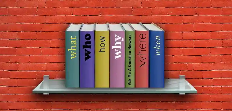 Books titled Who, What, Where, When, Why and How on a red wall bookshelf, symbolising the Ask Me A Question Network and its focus on different kinds of questions.